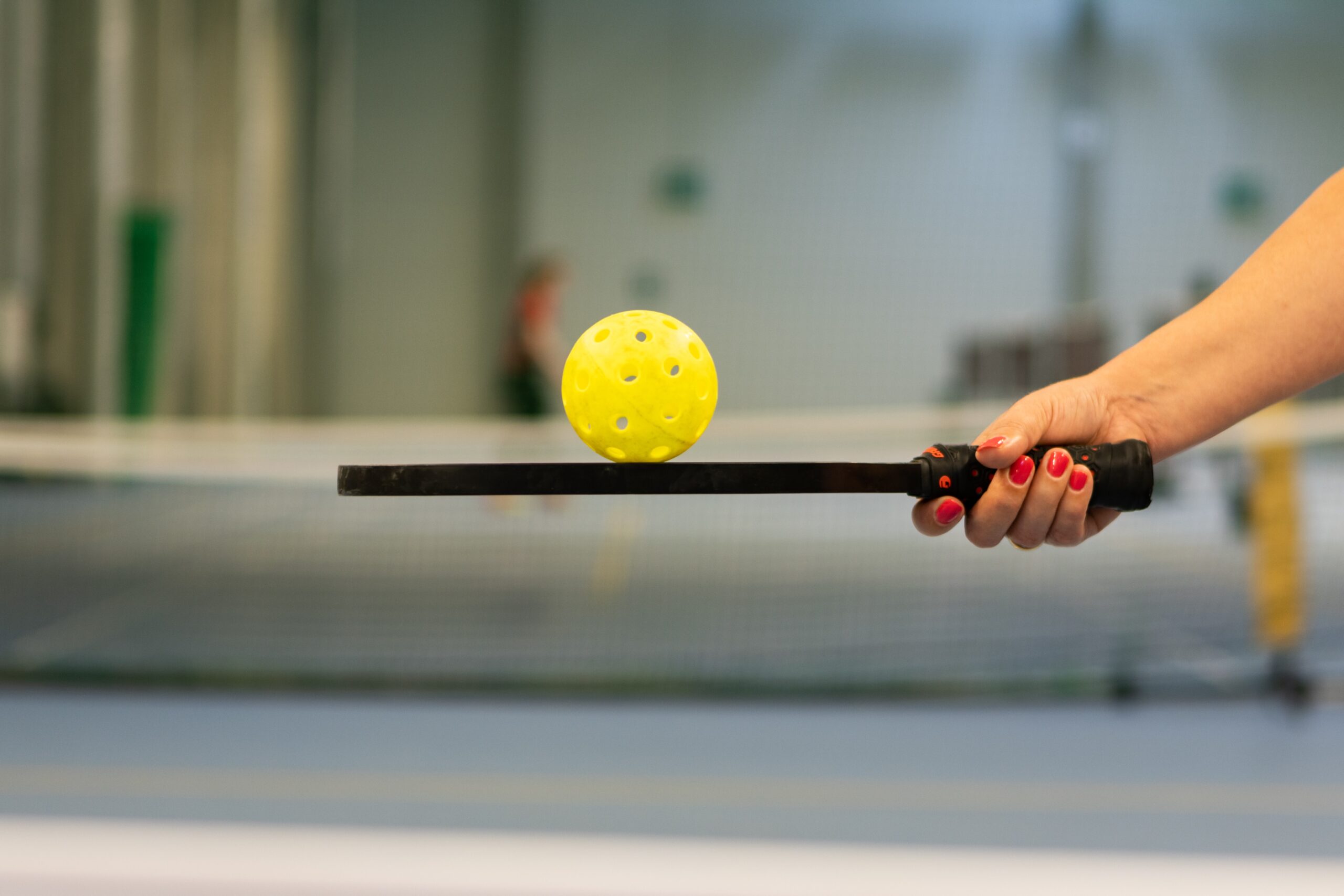 person holding a pickleball paddle while balancing a pickleball on it